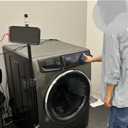 A participant presses the washer control panel while a camera on a stand records the session